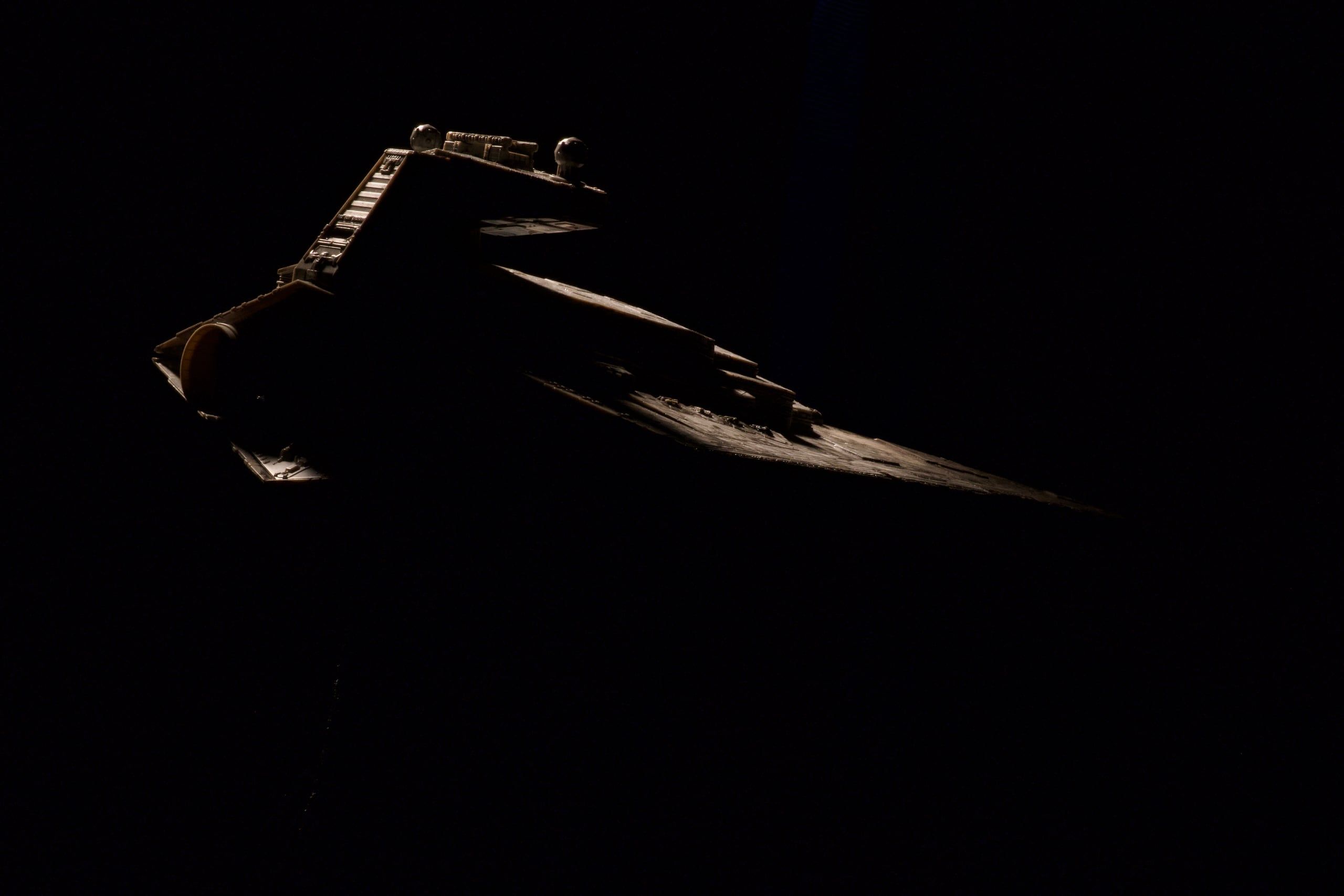 The starship miniature against black, lit from one side so only the edges of the hull catch light.