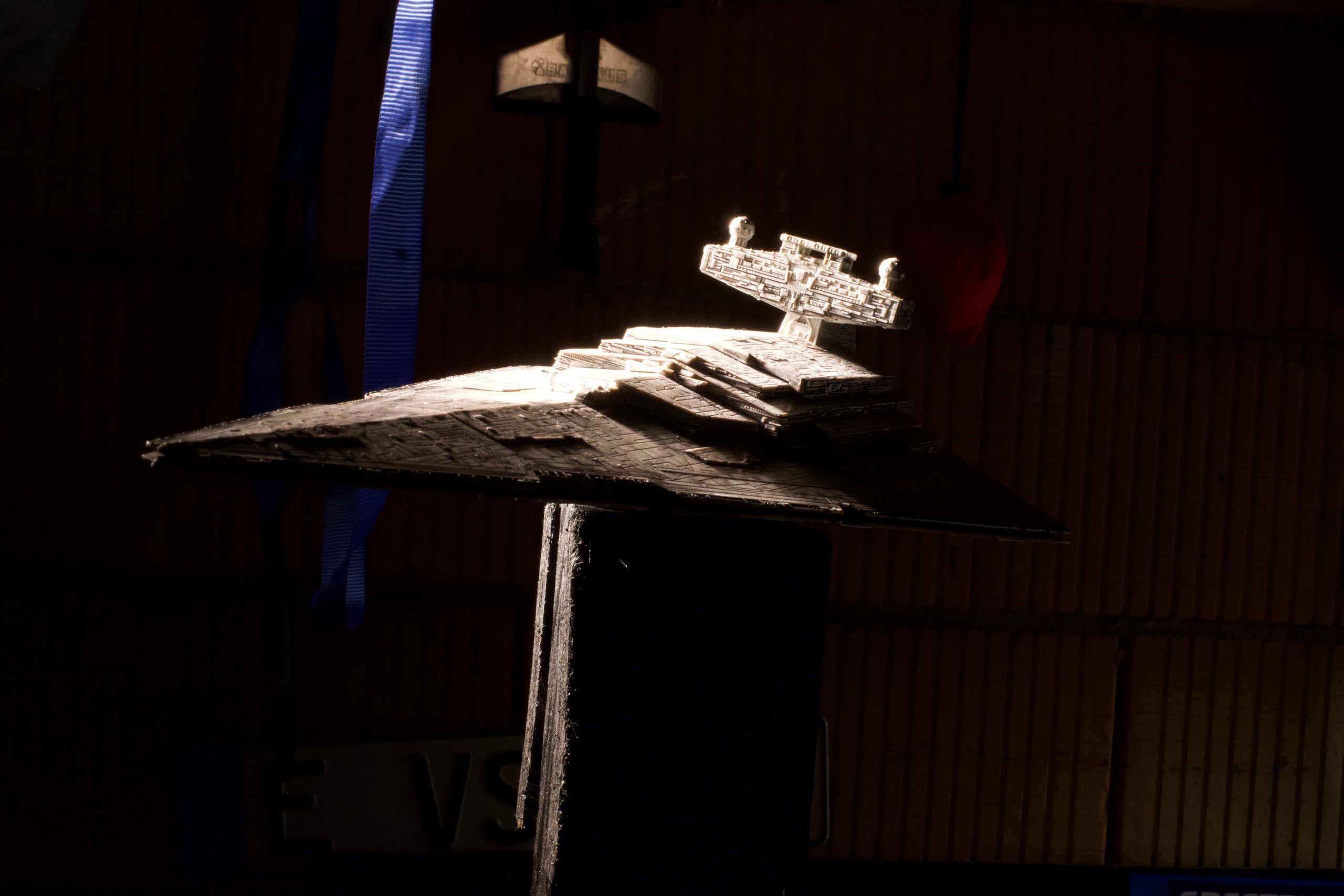 The starship miniature on its stand in the workshop, lit by a single hard key light.
