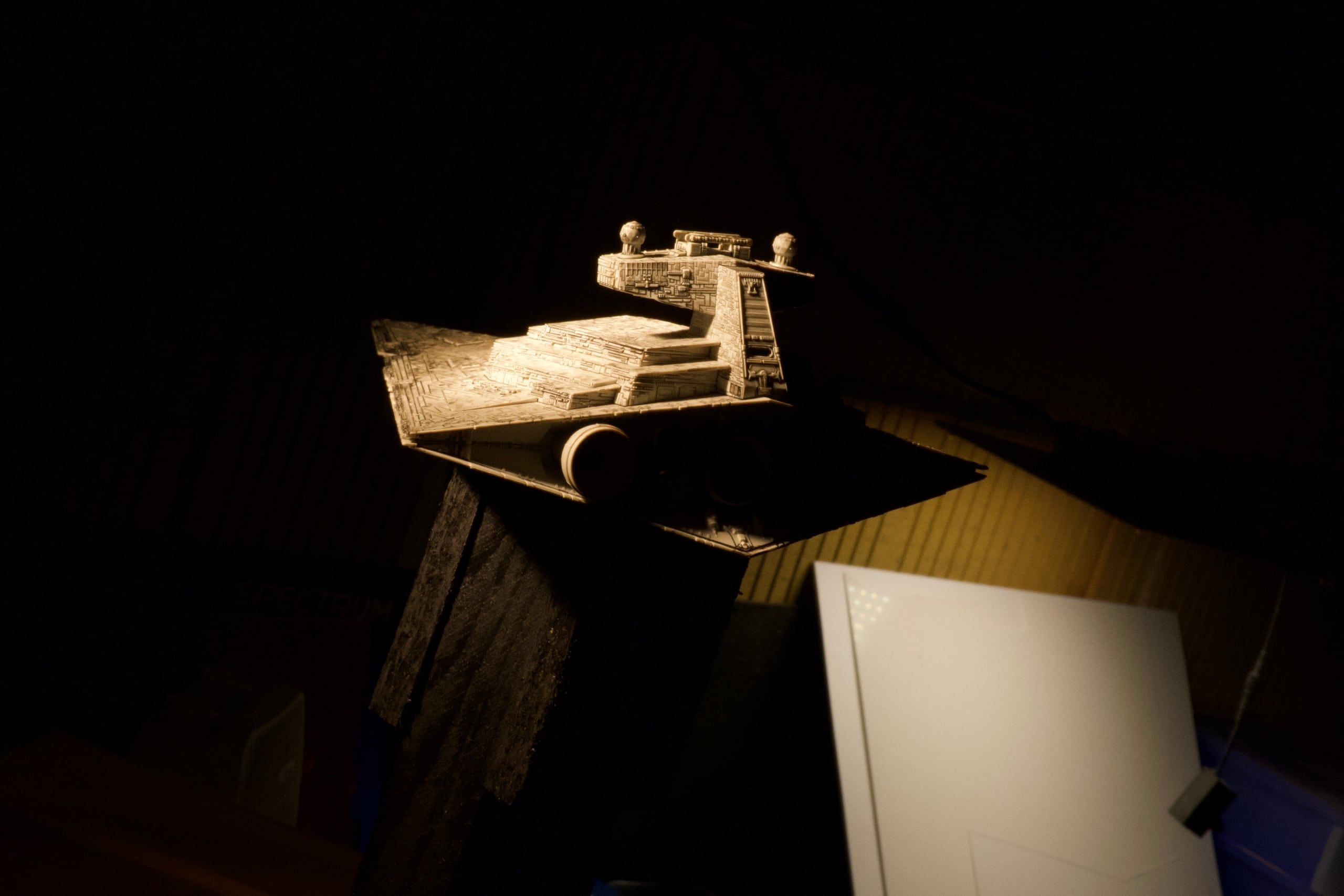 The bridge tower of the miniature, lit warm from above, the workshop wall behind it.
